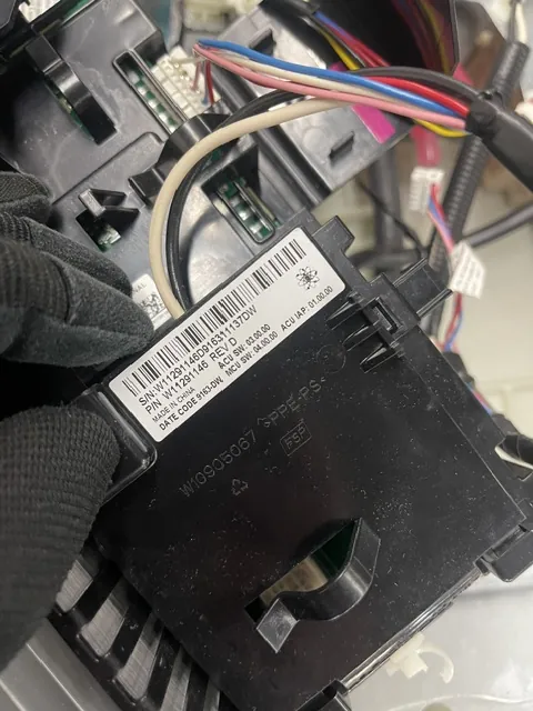 Gloved hand holding an appliance control module showing its part-number label