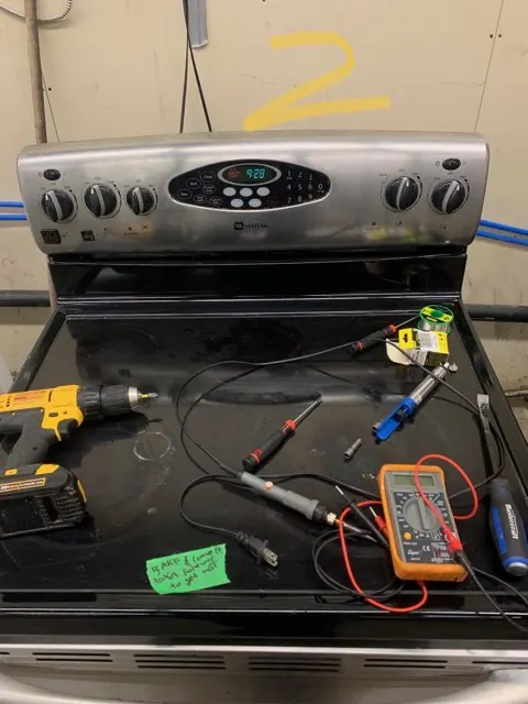 Electric range cooktop with meters and tools laid out for testing