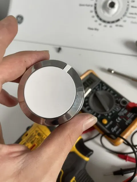 Selector knob removed from a laundry console, multimeter in the background